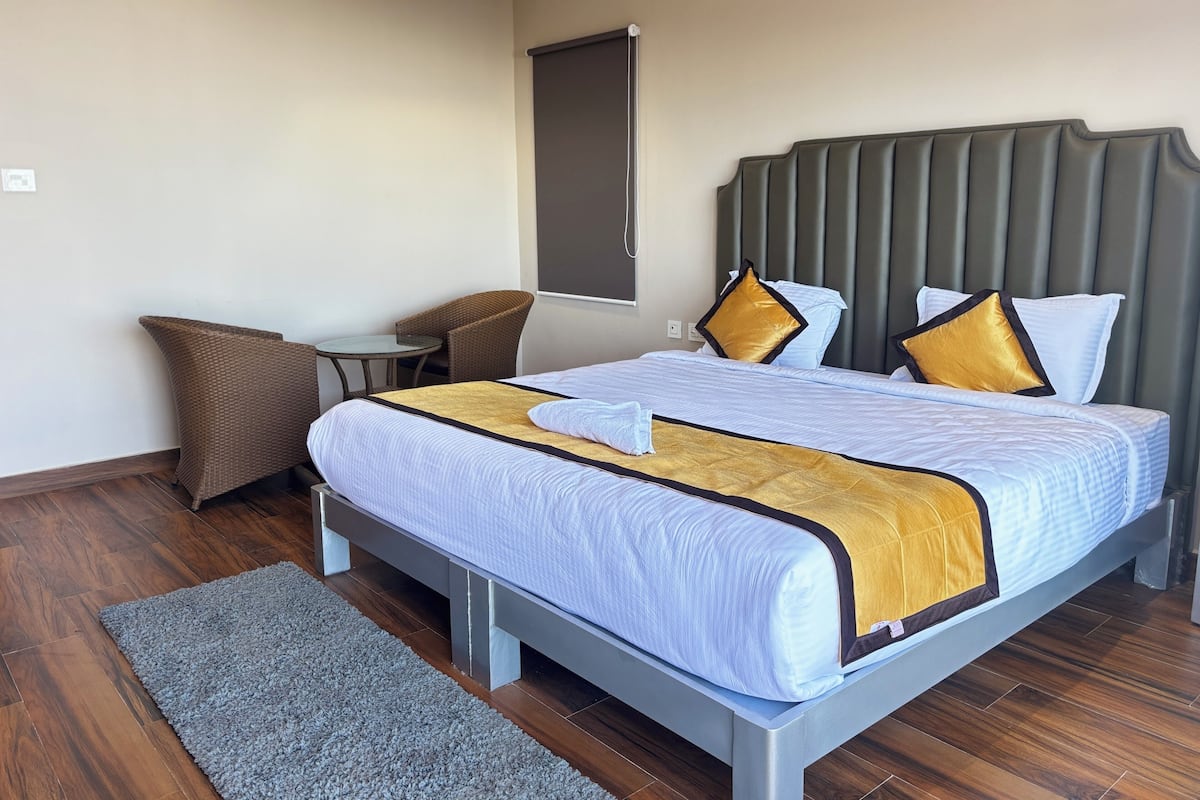 A hotel room with a bed, a small round table, a chair, and a large window.