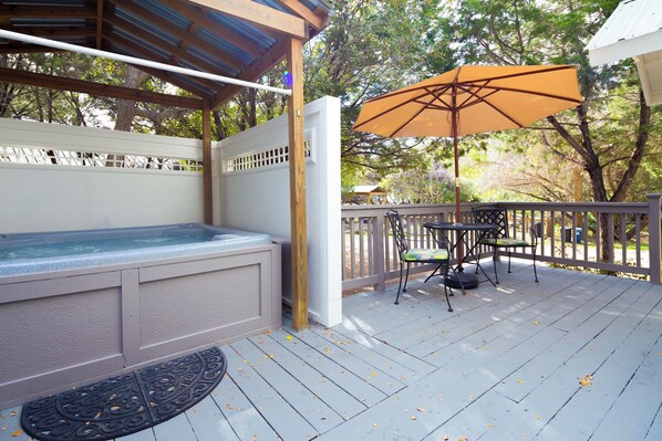 A covered outdoor deck with a hot tub, a table with chairs, and an umbrella.