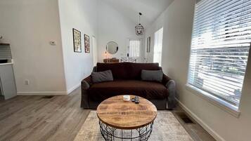 A living room with a sofa, a coffee table, and a window with blinds.