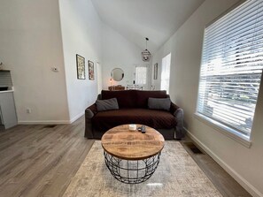 A living room with a sofa, a coffee table, and a window with blinds.