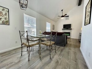 A modern living room with a dining area, a TV mounted on the wall, and a ceiling fan. - Cottage 2 Yellow, Pet-Friendly One-Bedroom Cottage, Private Hot Tub (Wimberley)