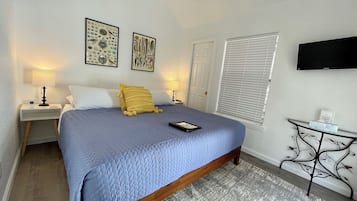 A bedroom with a bed, bedside tables, a TV, and artwork on the walls.