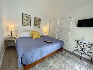 A bedroom with a bed, bedside tables, a TV, and artwork on the walls. - Cottage 2 Yellow, Pet-Friendly One-Bedroom Cottage, Private Hot Tub (Wimberley)