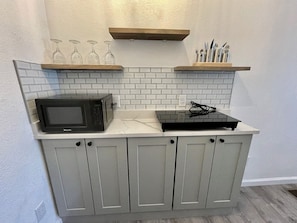 A kitchen with a microwave, a toaster, and wine glasses on a shelf. - Cottage 2 Yellow, Pet-Friendly One-Bedroom Cottage, Private Hot Tub (Wimberley)
