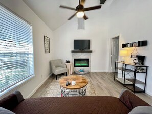 A modern living room with a fireplace, a television, and a ceiling fan.