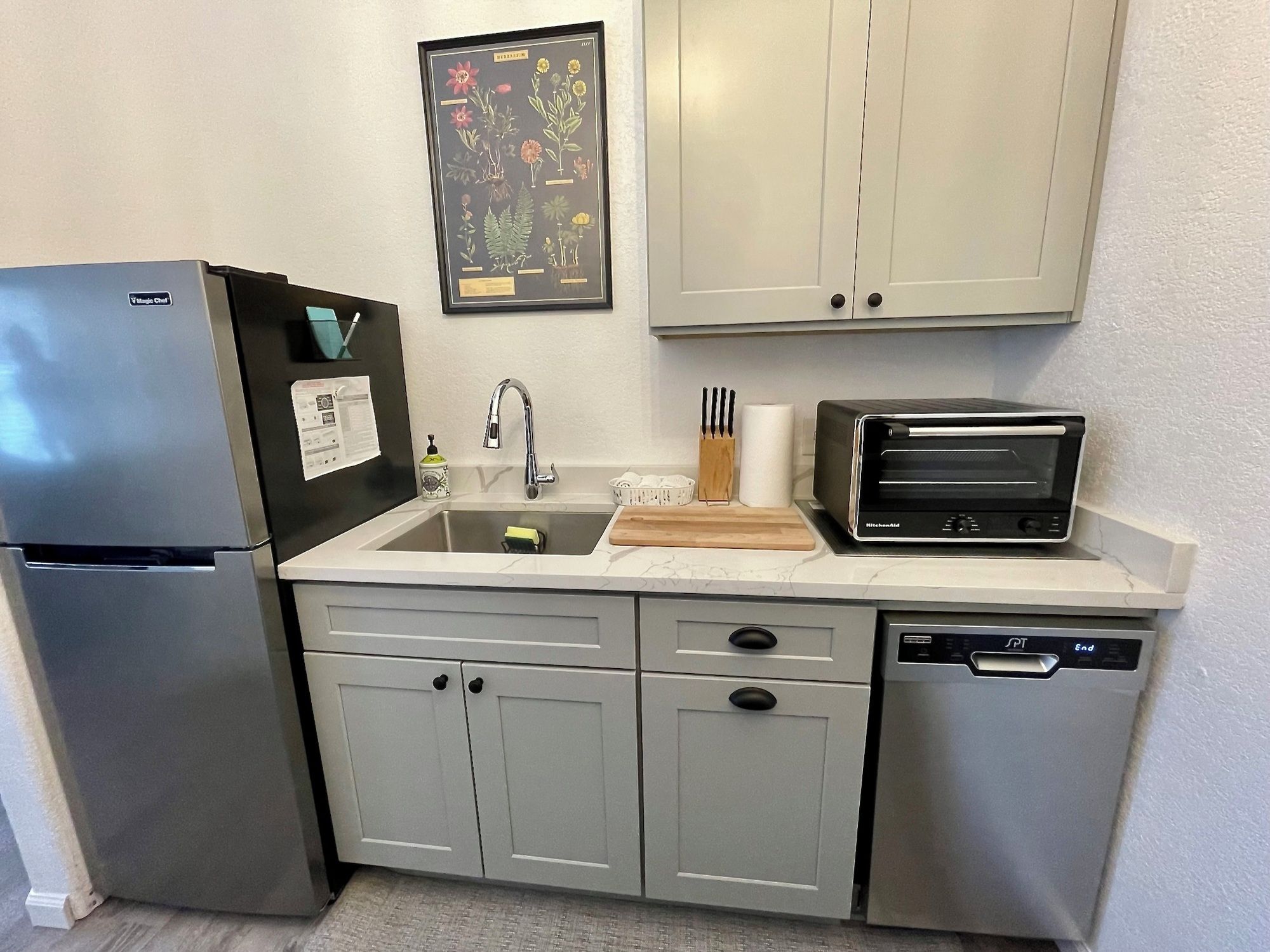 A compact kitchen with a refrigerator, sink, toaster, and dishwasher.