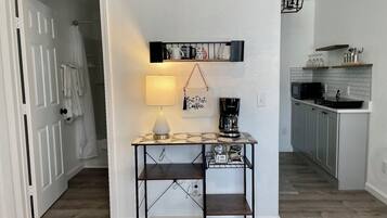 A hallway with a table, a hanging sign, a lamp, and a kitchen area with cabinets and a microwave.
