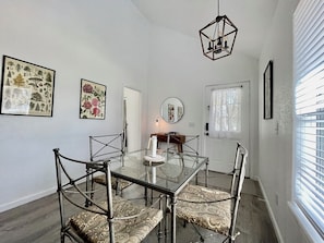 A dining area with a glass table surrounded by chairs, a hanging light fixture, and framed botanical prints on the walls.
