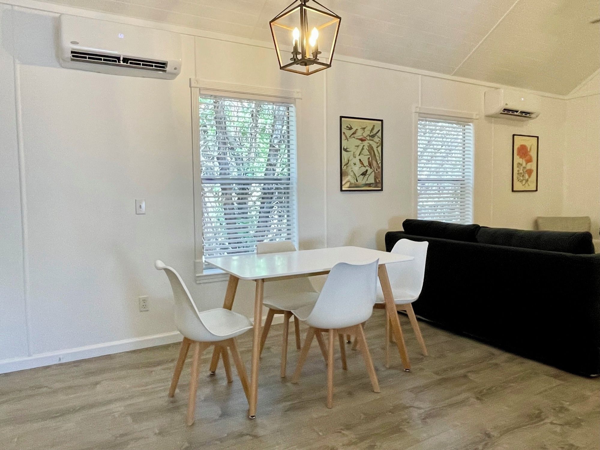 A dining area with a white table and chairs, a black sofa, and a ceiling light fixture.
