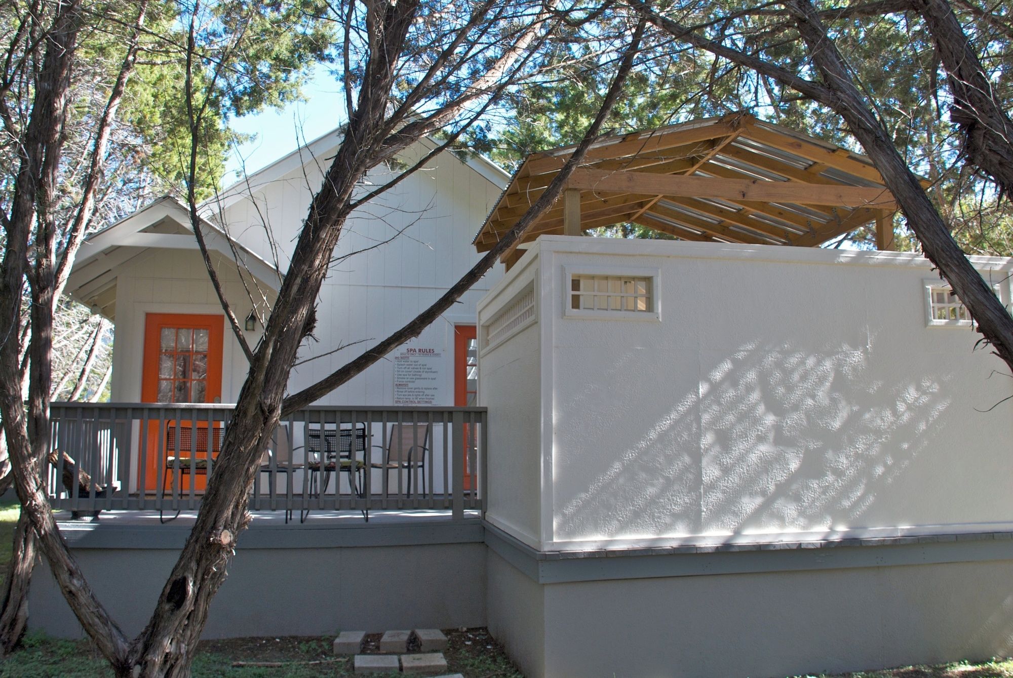 A building with a white exterior, a wooden roof structure, and a fenced outdoor area with a bench.