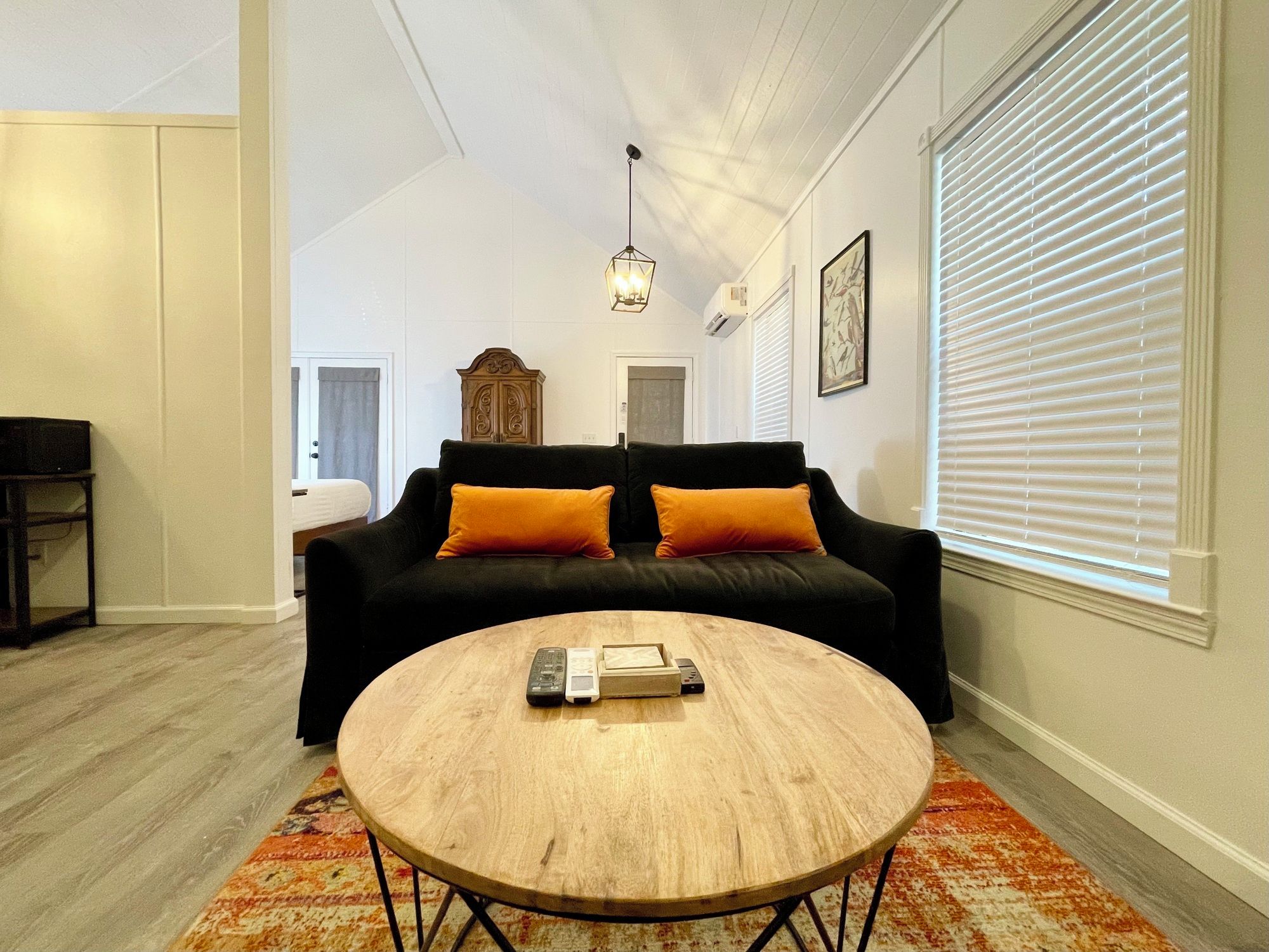 A living room with a black sofa, two orange cushions, a wooden coffee table, and a patterned rug.