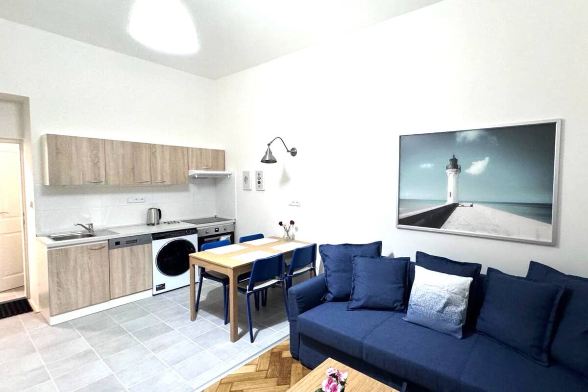 A compact living space with a kitchenette, a dining area, and a sofa with a view of a lighthouse.