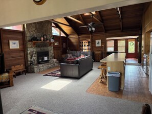 A log cabin interior with a stone fireplace, a sofa, a dining area, and a kitchen.