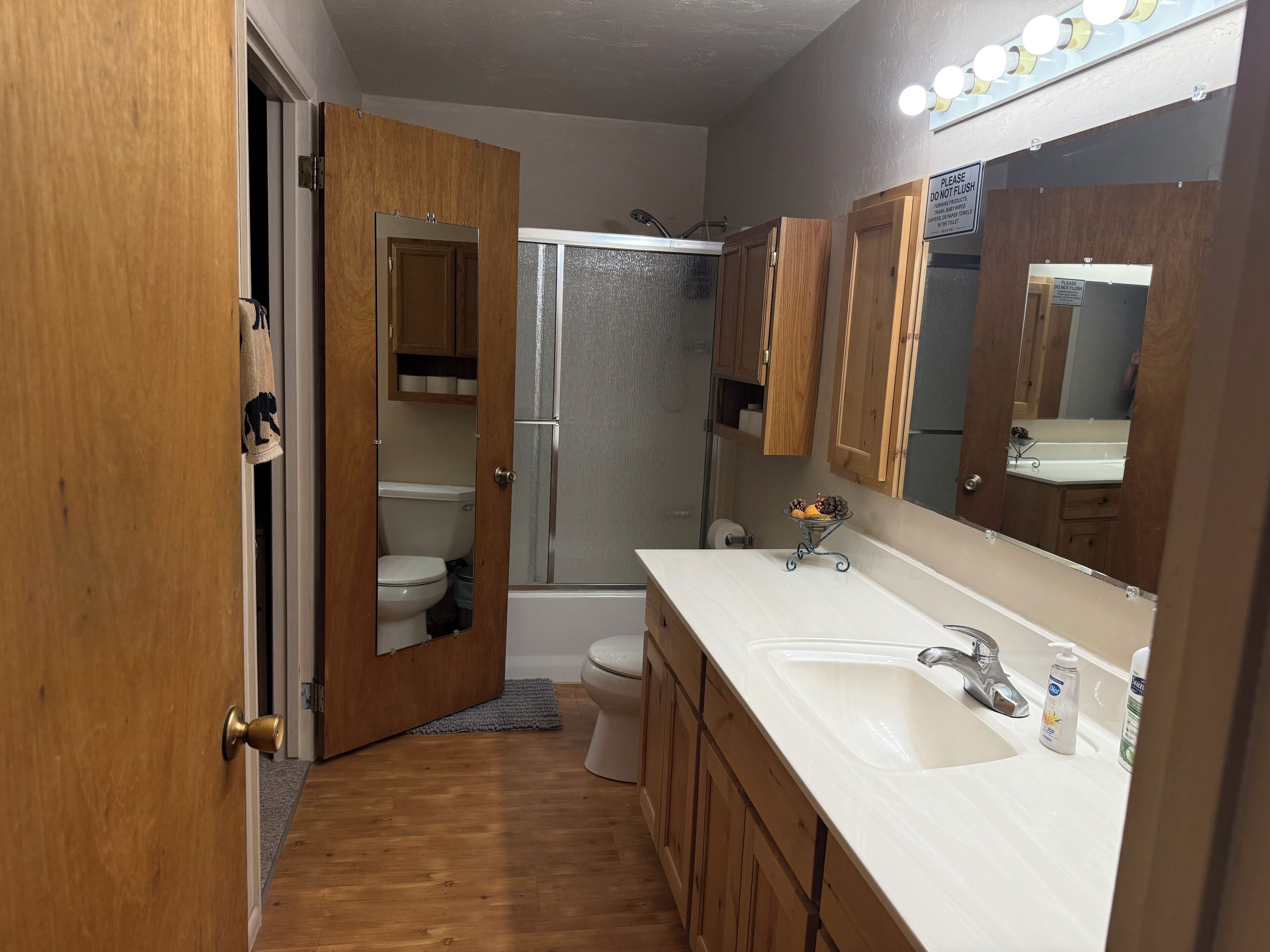 A bathroom with a wooden vanity, a sink, a mirror, and a shower area.