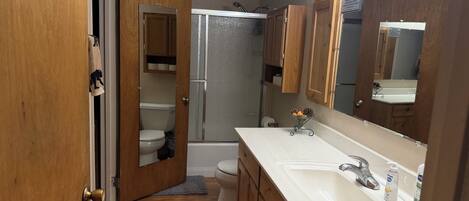 A bathroom with a wooden vanity, a sink, a mirror, and a shower area.