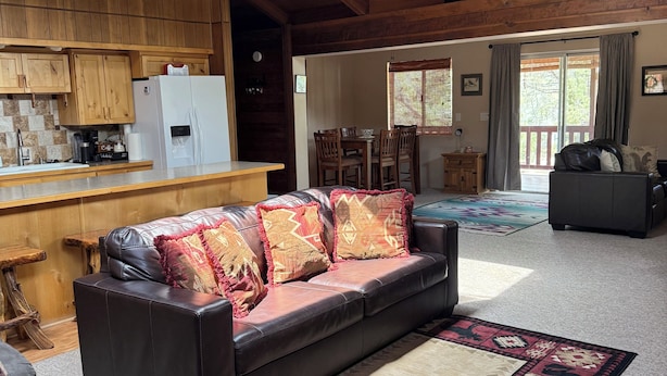 A spacious living area with a leather sofa, a dining table, and a kitchen with wooden cabinets. - Heber in the Woods/Hot Tub/4% wkly discount/Hiking (Heber-Overgaard)