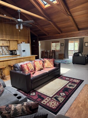 A spacious living area with a leather sofa, a dining table, and a kitchen with wooden cabinets.
