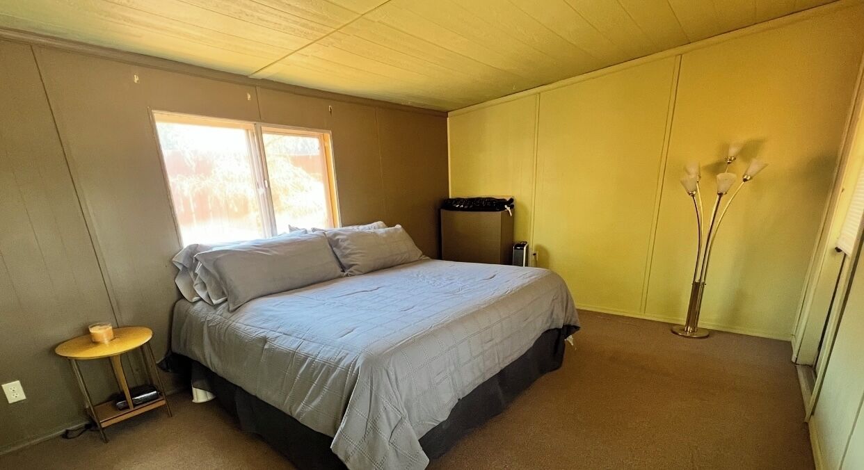 Une chambre à coucher avec un lit, une table de chevet, une lampe et une fenêtre.