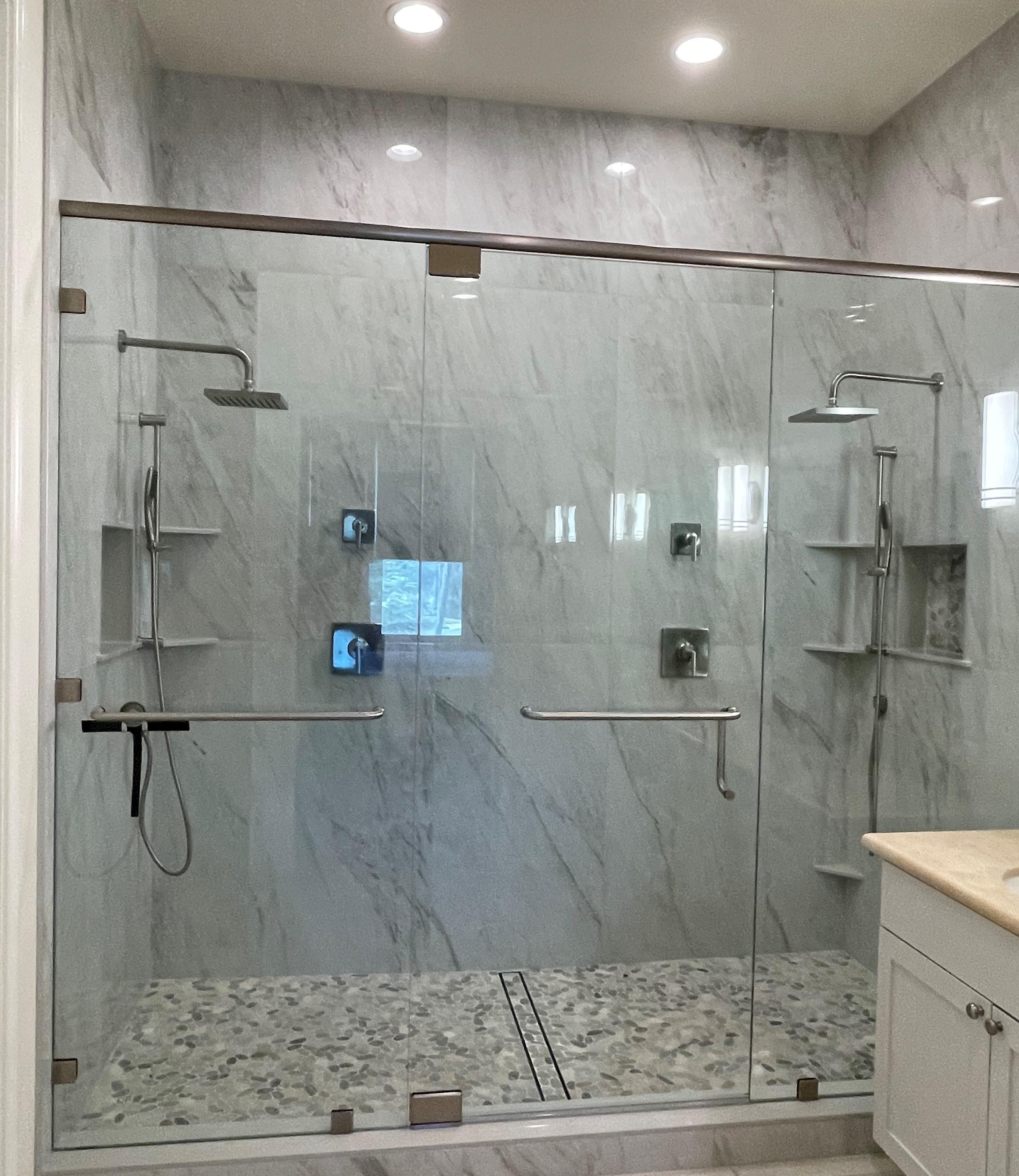 A glass-enclosed shower area with a marble floor, a handrail, and a control panel.