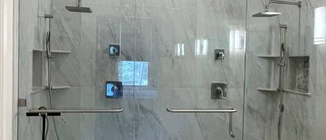 A glass-enclosed shower area with a marble floor, a handrail, and a control panel.