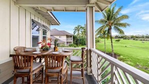 A wooden dining table with chairs on a covered porch overlooking a green landscape with palm trees. - Fairway Villas Waikoloa G31 (Waikoloa)