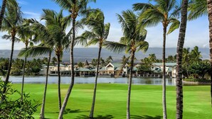 A golf course with palm trees and a view of a lake and buildings in the background. - Fairway Villas Waikoloa G31 (Waikoloa)