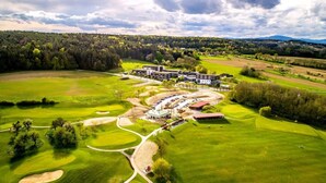 An aerial view of a golf course with a clubhouse, multiple buildings, and surrounding forested areas.