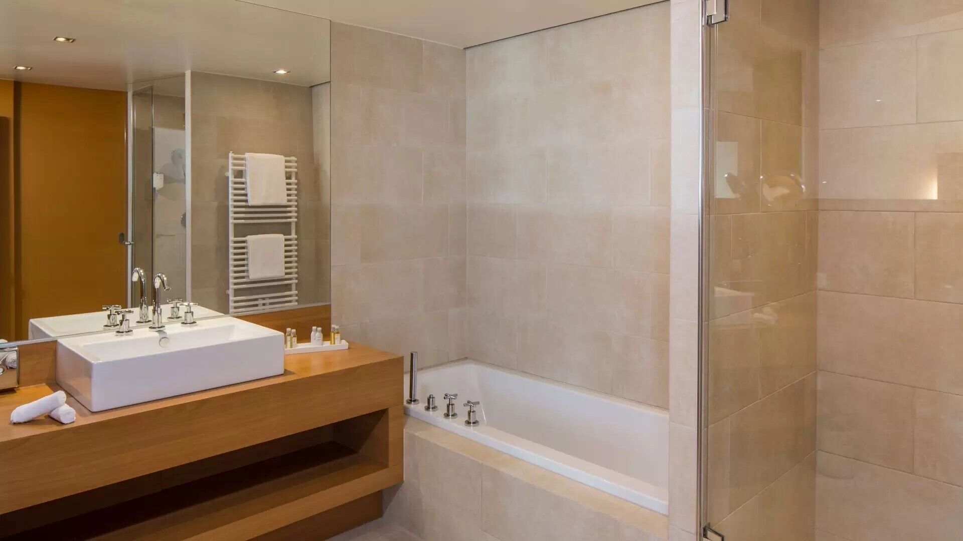 A modern bathroom with a large mirror, a white sink, a bathtub, and a glass shower enclosure.