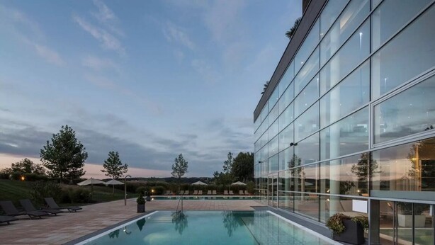 A modern building with a glass facade, a swimming pool, and outdoor seating.
