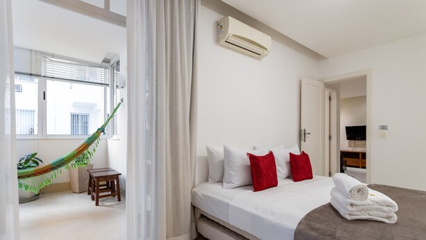 A hotel room with a bed, a hammock, a small table, and a window with blinds. - 4 minutes from Copacabana beach | NSC205 (Rio de Janeiro)