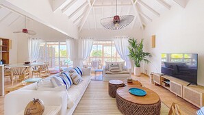 A spacious living room with a high ceiling, a large TV, and a balcony with outdoor seating.