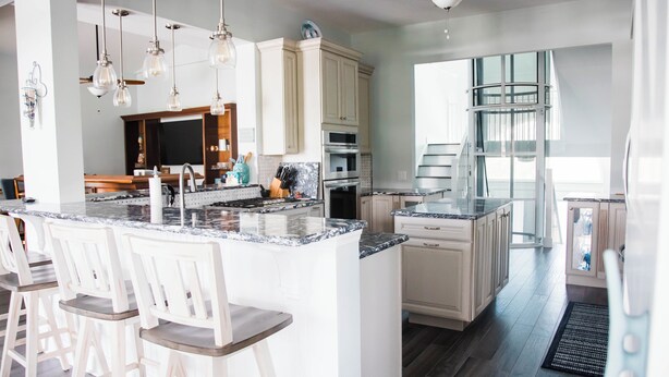 A modern kitchen with white cabinets, a central island with bar stools, and a large window providing natural light. - Luxurious Large Home on Gulf of Mexico w/Private 30' Dock (Englewood)