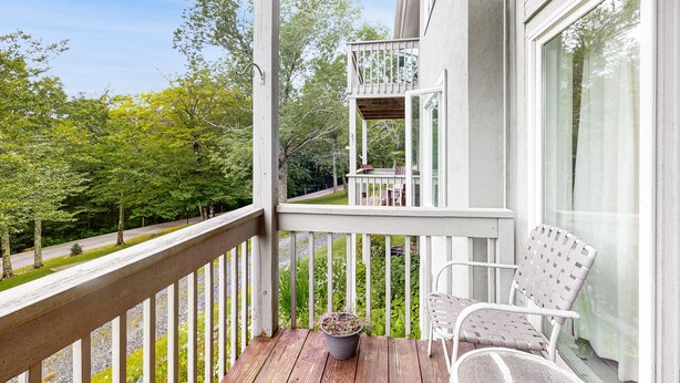 A wooden deck with a potted plant, a white chair, and a view of a road and trees. - Cozy Mountain Retreat: Single-Level Condo in Sugar Mountain with Modern Comforts (Sugar Mountain)