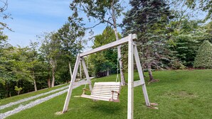 A wooden swing set in a grassy area with trees in the background. - Cozy Mountain Retreat: Single-Level Condo in Sugar Mountain with Modern Comforts (Sugar Mountain)