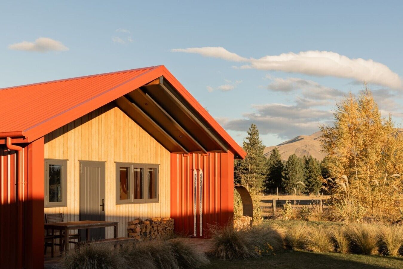 A wooden cabin with a red roof, a dining area, and a view of mountains and trees.