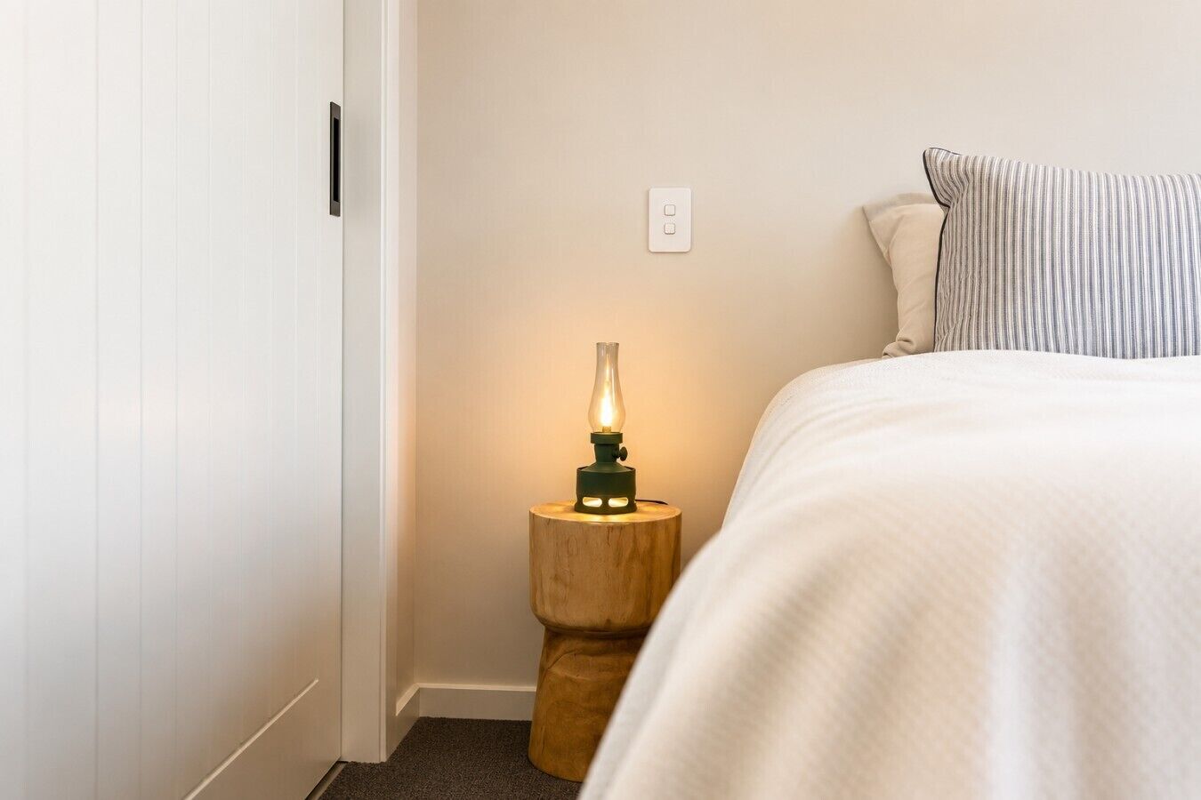 Une chambre à coucher avec un lit, une table de chevet avec une lampe, une prise de courant et une porte.