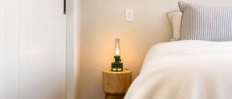 A bedroom with a bed, a bedside table with a lamp, a wall socket, and a door.