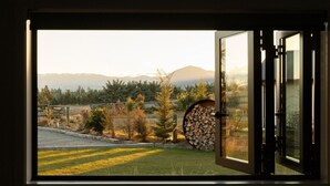 Vista a través de una puerta abierta que da a un cuarto con ventana, desde donde se ve un espacio cubierto de pasto, árboles y montañas.