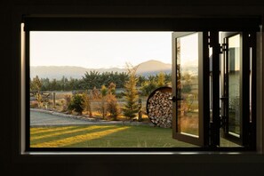 A view through an open door of a room with a window overlooking a grassy area, trees, and mountains.