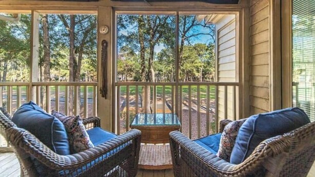 A covered porch with wicker furniture and a glass table, overlooking a wooded area. - Our Li'l Getawave! Two-bedroom condo in Pawleys Plantation Golf and Country Club (Pawleys Island)