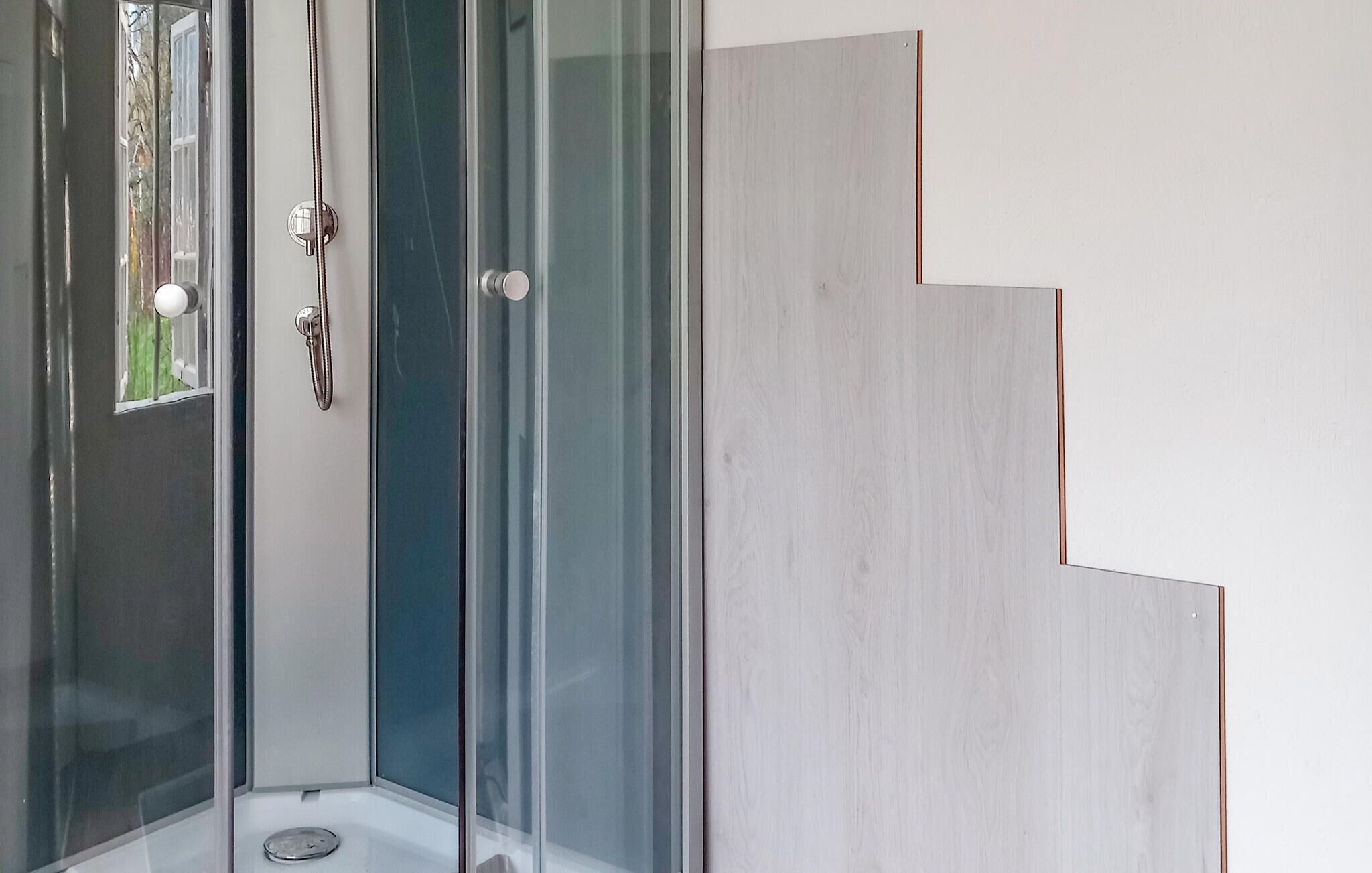 Un coin de pièce avec une porte en verre, une poignée en métal et un panneau en bois orné d’un motif évoquant un escalier.