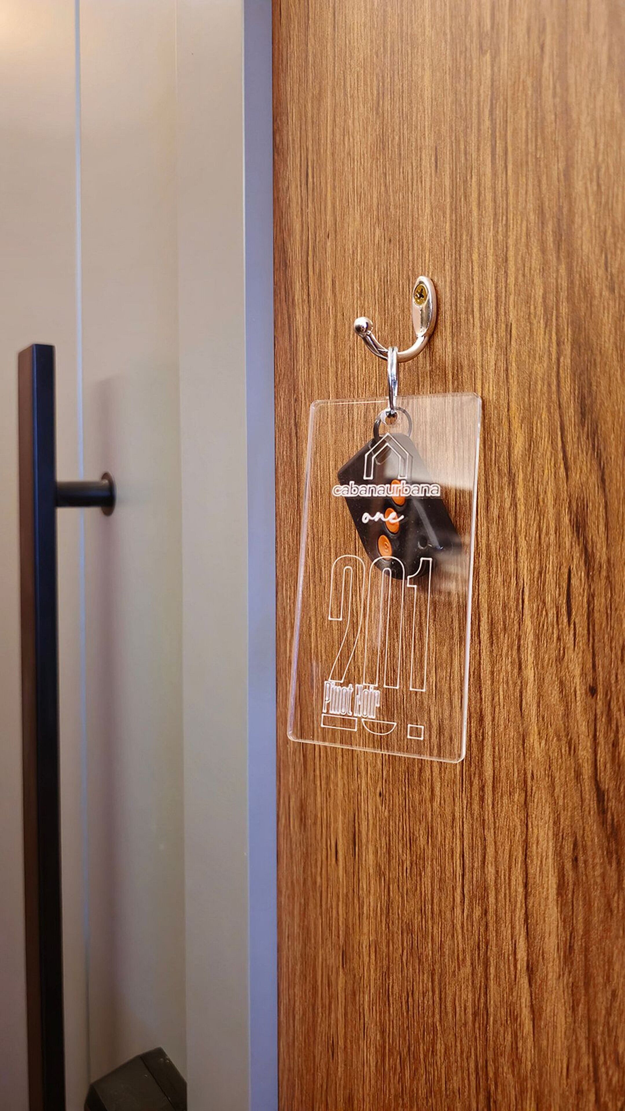 Uma porta de madeira com um gancho de metal e uma placa de plástico transparente com texto e um logotipo.