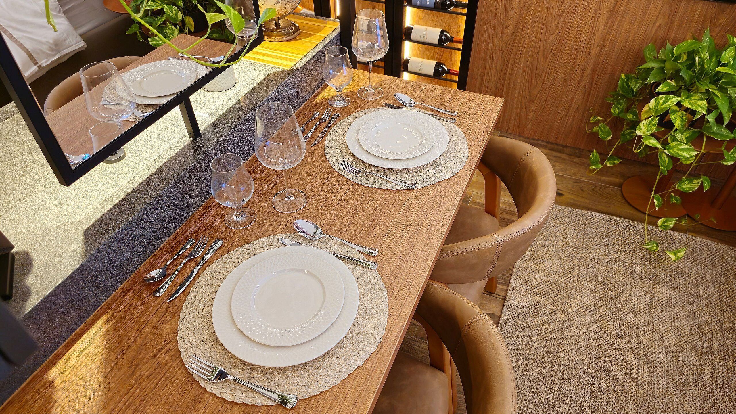 A dining table set with plates, cutlery, and wine glasses, with a mirror reflecting the table.