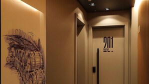 A hallway with a framed artwork on the left, a door with the number 201, and a light fixture on the ceiling. - Pinot Noir Cabin - Urban Cabin (Bento Gonçalves)