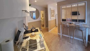 A modern kitchen with a built-in oven, a microwave, and a coffee machine. There is a small dining area with a table and chairs. - The White cosy, maxi studio in the city center, 1 km from the train station, tourism/business (Calais)