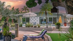 Un espace aménagé au bord de la piscine, avec des chaises longues, des parasols et une vue sur une maison dotée d’une piscine.