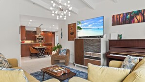 Un salon moderne comprenant un canapé, une table basse, un téléviseur, un piano et un coin repas avec des chaises et une table.