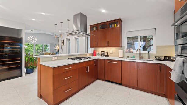 A modern kitchen with wooden cabinets, a central island, and a built-in oven. - Villa Piano (Fort Lauderdale)