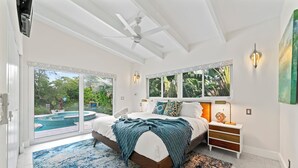 A bedroom with a large bed, a nightstand, a lamp, and a view of a swimming pool through glass doors. - Villa Piano (Fort Lauderdale)