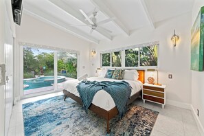 A bedroom with a large bed, a nightstand, a lamp, and a view of a swimming pool through glass doors. - Villa Piano (Fort Lauderdale)
